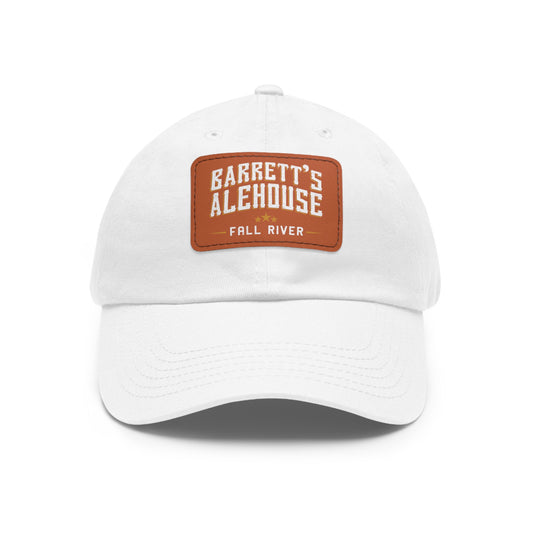 White unstructured dad hat with a brown faux leather patch featuring the Barrett's Alehouse Fall River logo.