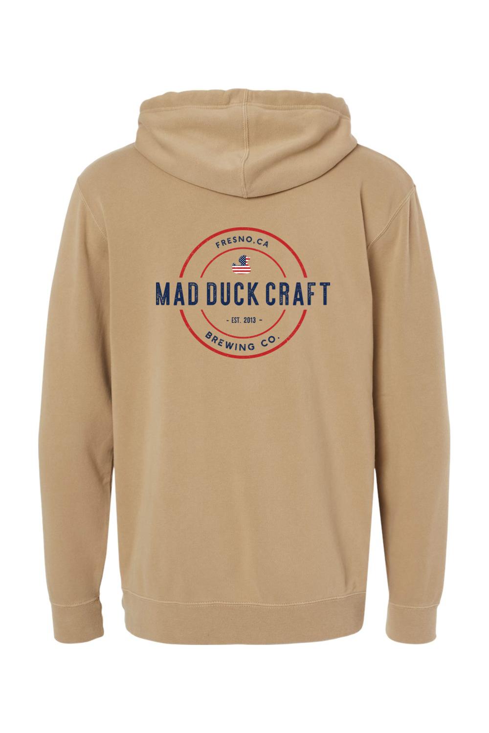 Tan pigment-dyed hoodie featuring a red, white, and blue Mad Duck Craft Brewing Co. logo on the back.
