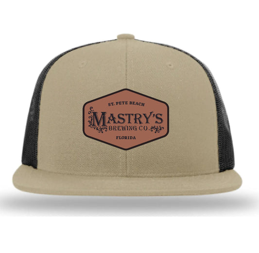 Tan snapback hat with a Mastry’s Brewing Co. leather patch, featuring a structured front and breathable black mesh back.