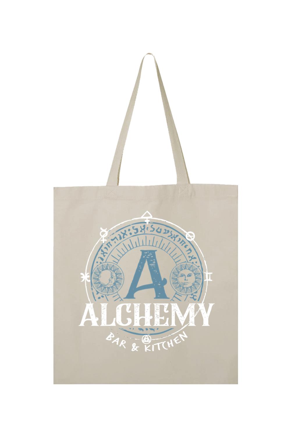 Beige canvas tote bag featuring a blue and white circular alchemy-themed graphic with sun, moon, and text.