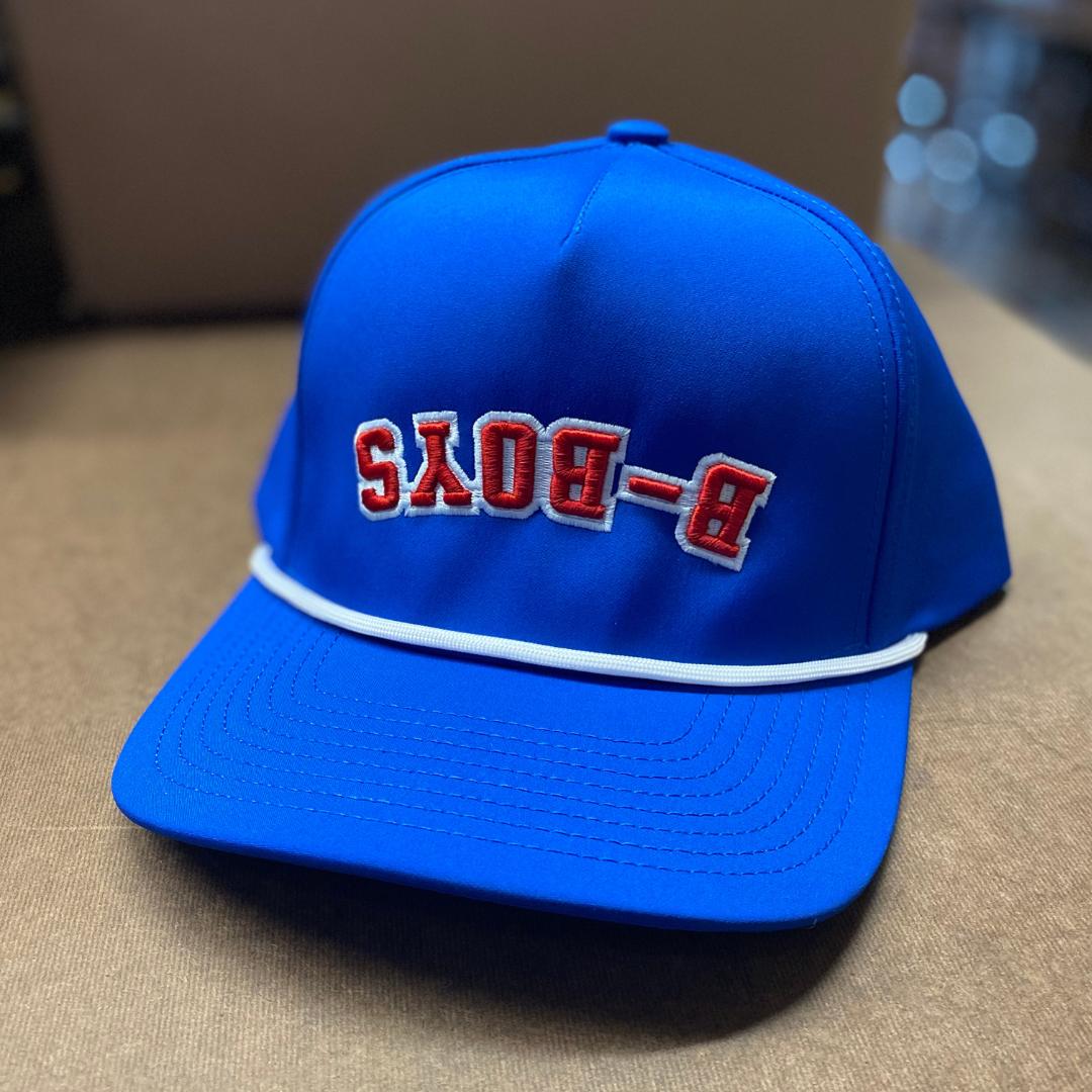 Bright blue snapback hat featuring reversed red B-BOYS embroidery and a decorative white rope across the brim.