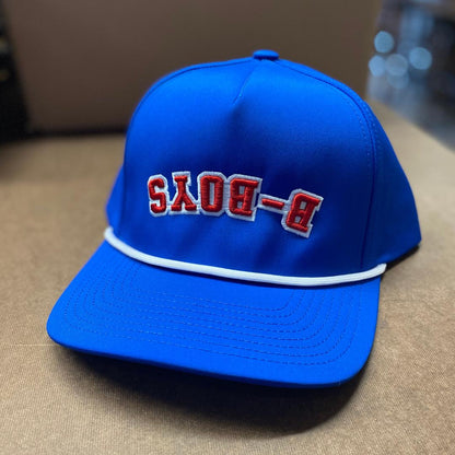 Bright blue snapback hat featuring reversed red B-BOYS embroidery and a decorative white rope across the brim.