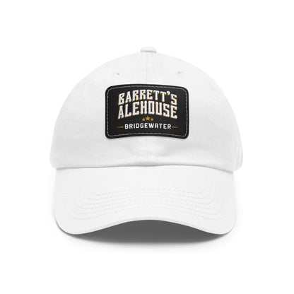 White bio-washed chino twill dad cap featuring a black faux leather patch with Barrett's Alehouse Bridgewater logo.