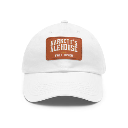 White unstructured dad hat with a brown faux leather patch featuring the Barrett's Alehouse Fall River logo.