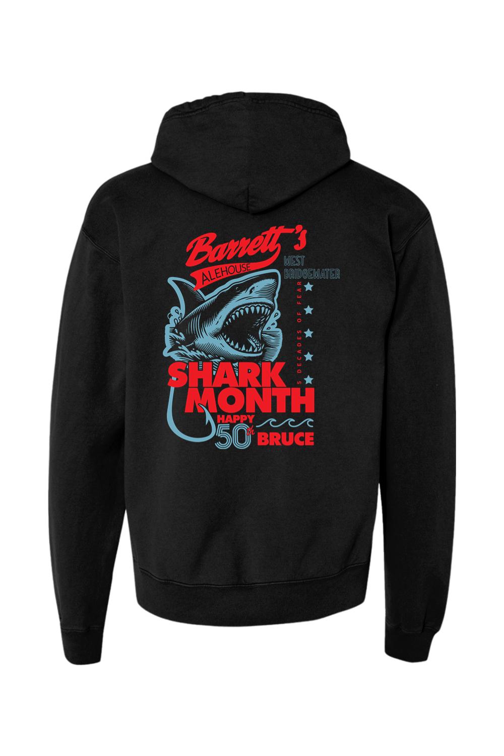 Black garment-dyed hoodie featuring a blue shark graphic and Barrett's Alehouse Shark Month 2025 text on the back.