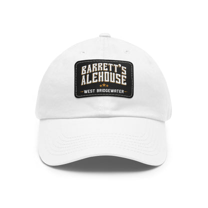 White unstructured dad hat with a black faux leather patch featuring the Barrett's Alehouse West Bridgewater logo.