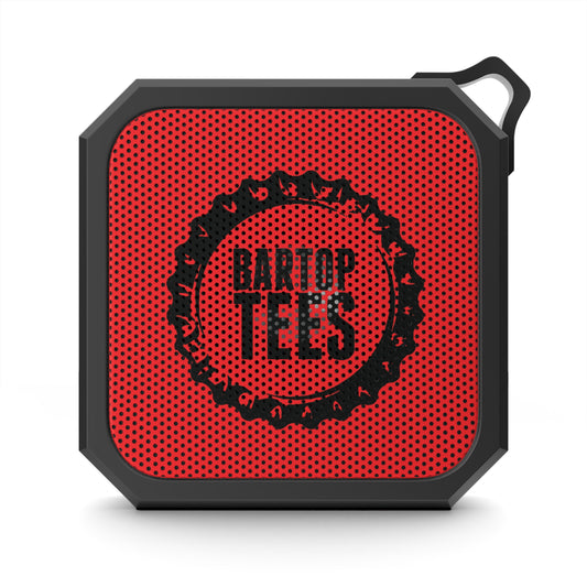 Compact red and black square outdoor Bluetooth speaker with a built-in carabiner clip and perforated grille design.