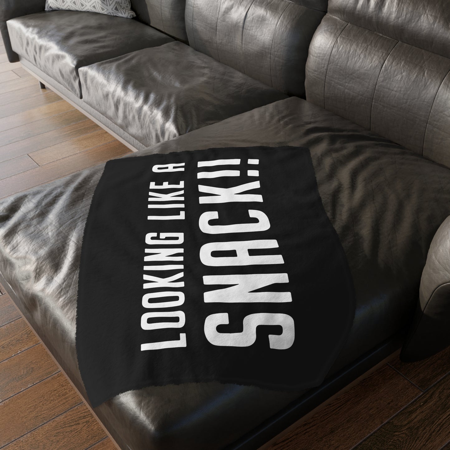 Soft black velveteen minky blanket with white Looking Like A Snack text, draped over a dark leather sofa.