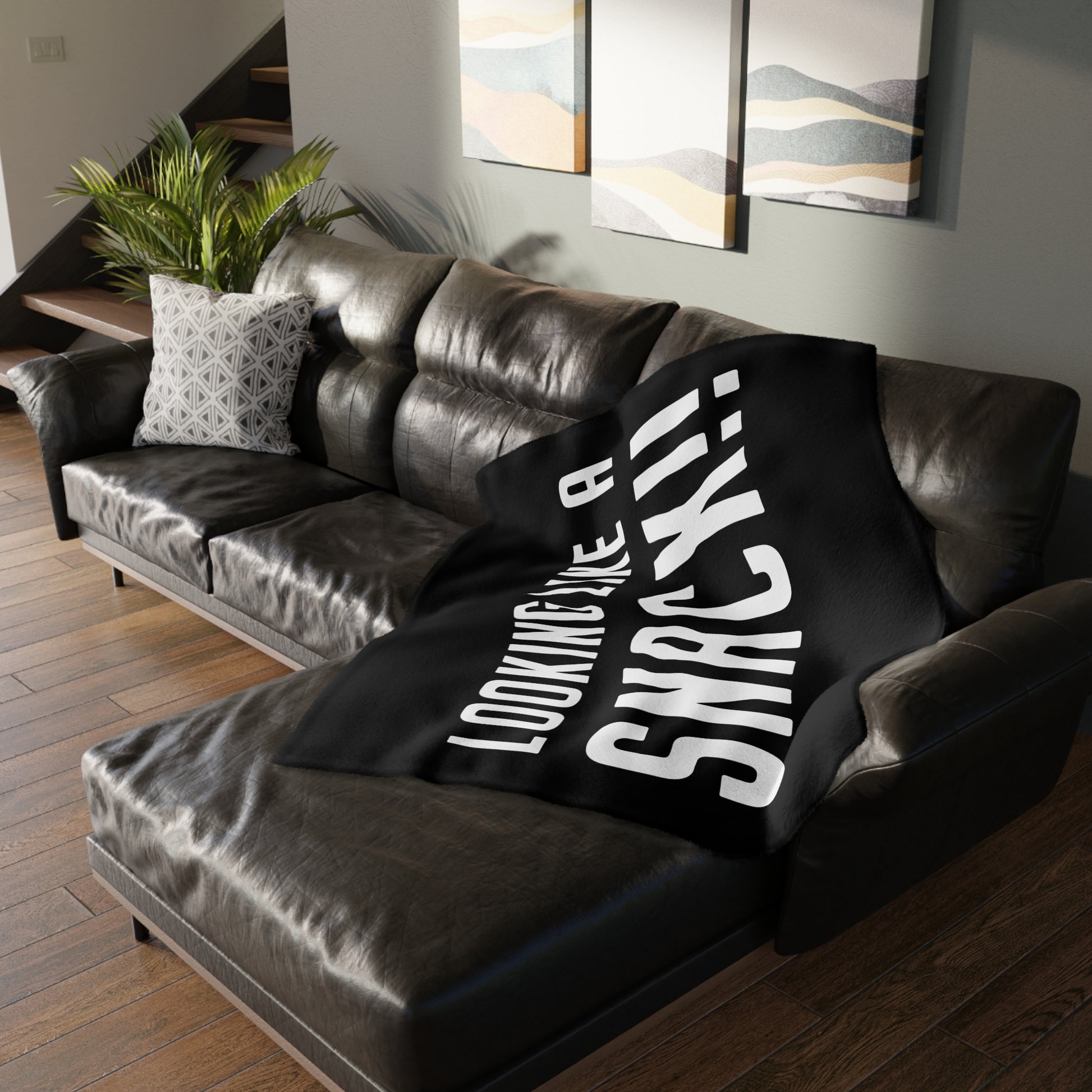 Soft black velveteen minky blanket with white Looking Like A Snack text draped over a dark leather sectional sofa.