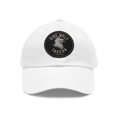 White unstructured dad hat with a round black PU leather patch featuring a Dire Wolf Tavern logo.