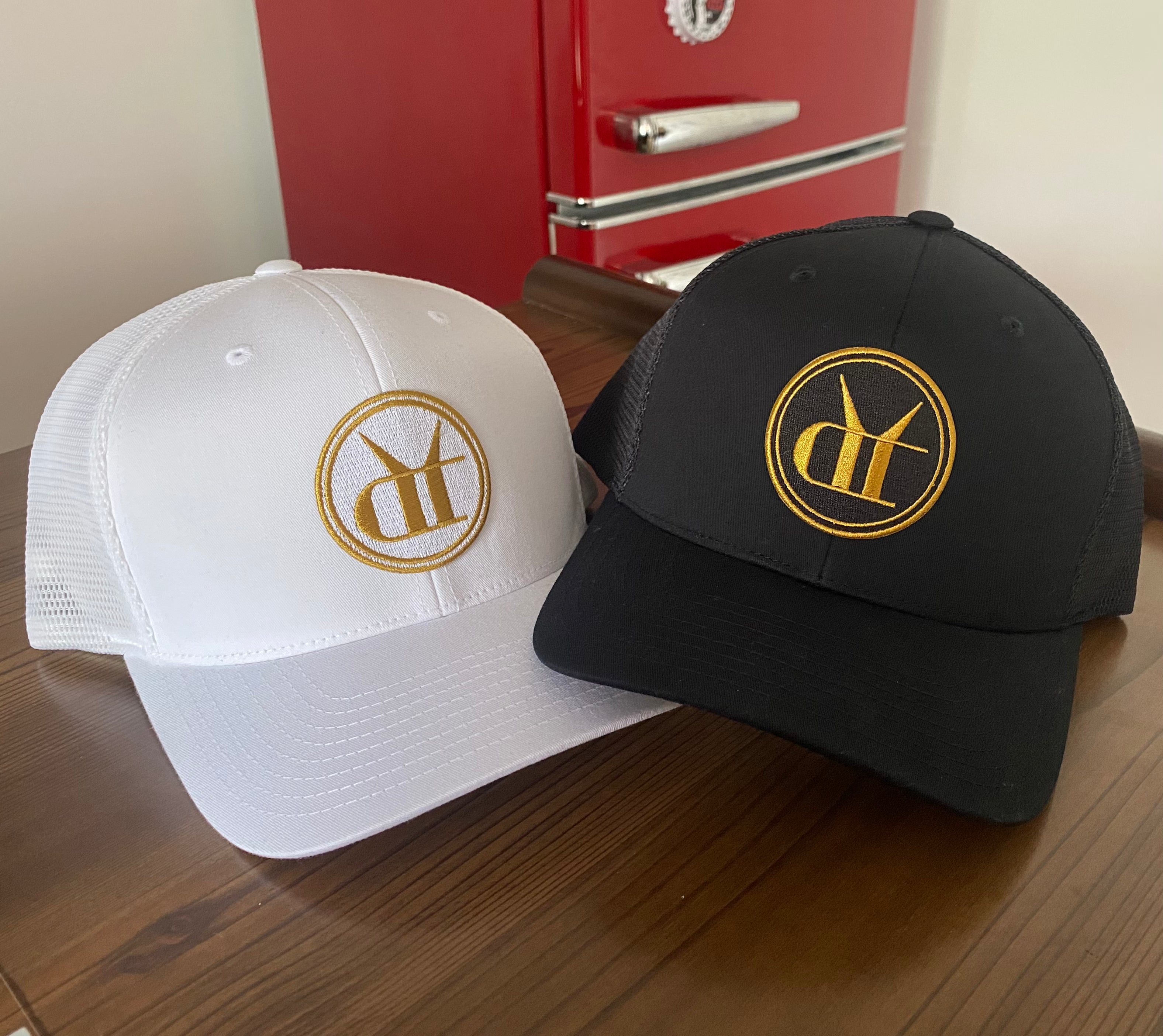 Black and white snapback trucker hats with gold embroidered circular logos and breathable mesh back panels.