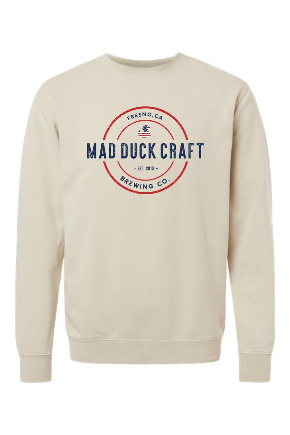 Beige pigment-dyed crewneck sweatshirt featuring a red, white, and blue Mad Duck Craft Brewing Co. logo graphic.