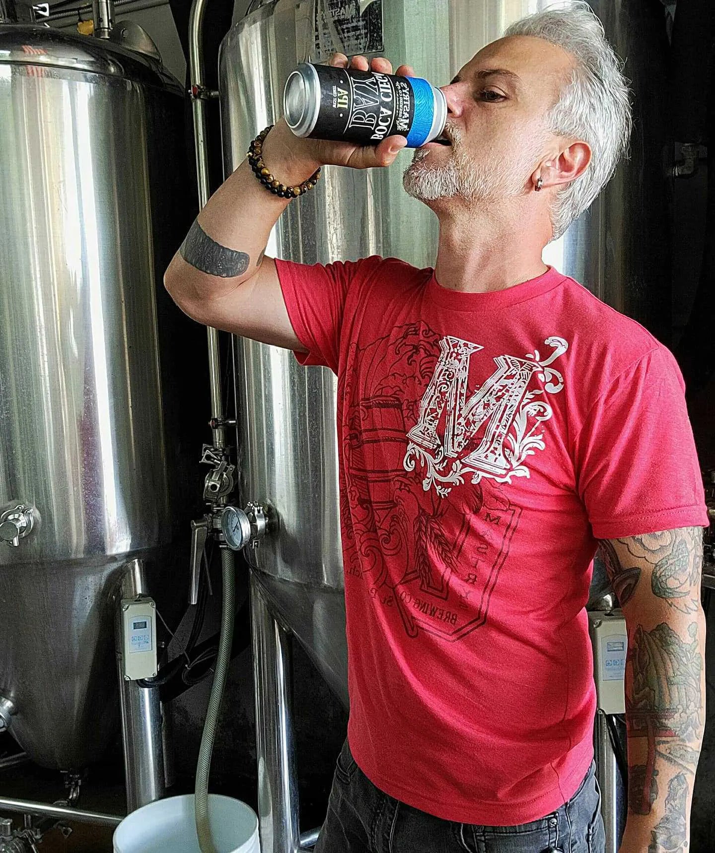 Man wearing a heather red Mastry’s Brewing Co. triblend graphic tee with a white collage logo design.
