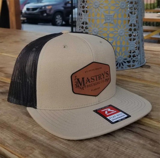 Tan and black mesh snapback hat featuring a brown leather Mastry’s Brewing Co. patch on the front.