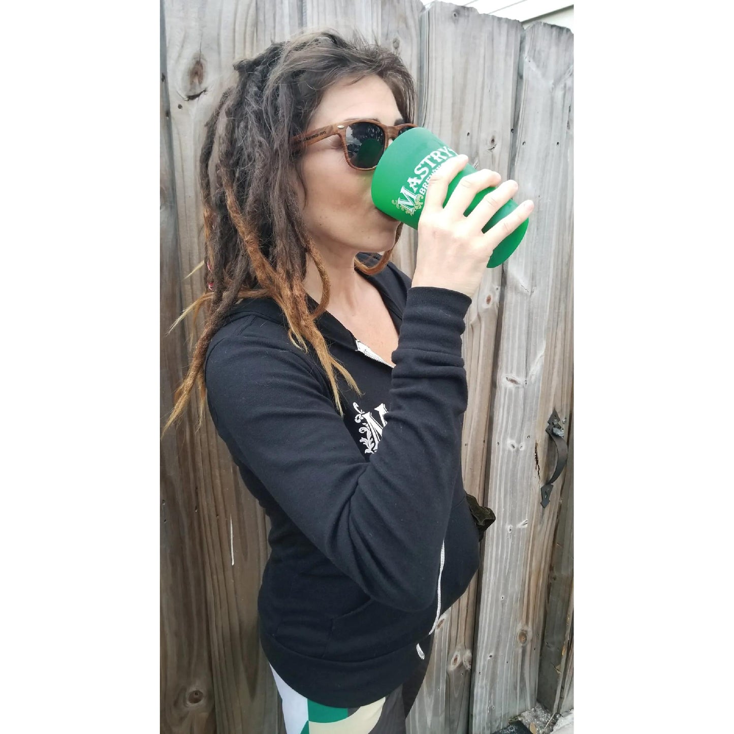 Woman wearing a black Mastry’s zip-up hoodie with a metal zipper, drinking from a green Mastry’s Brewing cup.