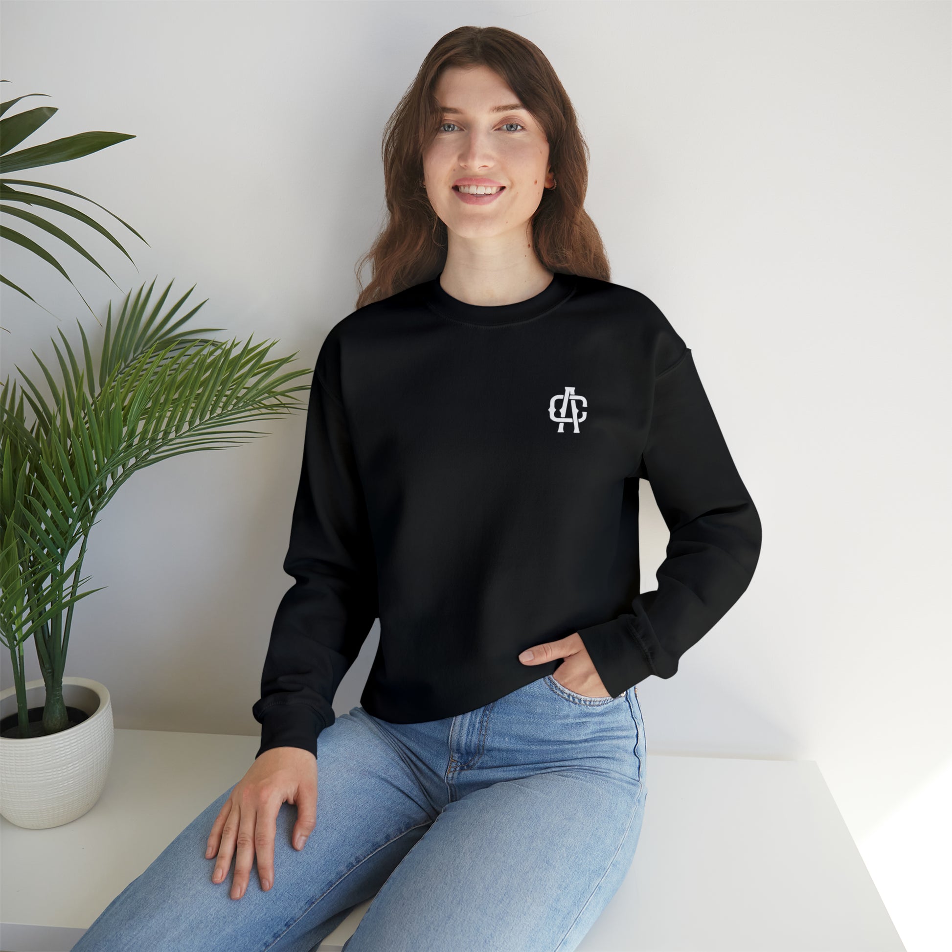 Woman wearing a black heavy blend crewneck sweatshirt with a small white logo on the chest and ribbed knit collar.