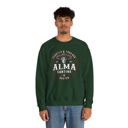 Man wearing a dark green heavy blend crewneck sweatshirt with a white and red Alma Cantina skull graphic.