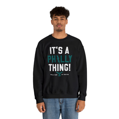 Man wearing a black heavy blend crewneck sweatshirt with It's A Philly Thing graphic print in white and teal.