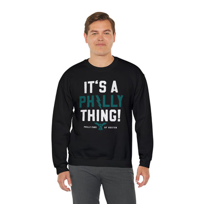 Man wearing a black heavy blend crewneck sweatshirt with It's A Philly Thing graphic print in white and teal.