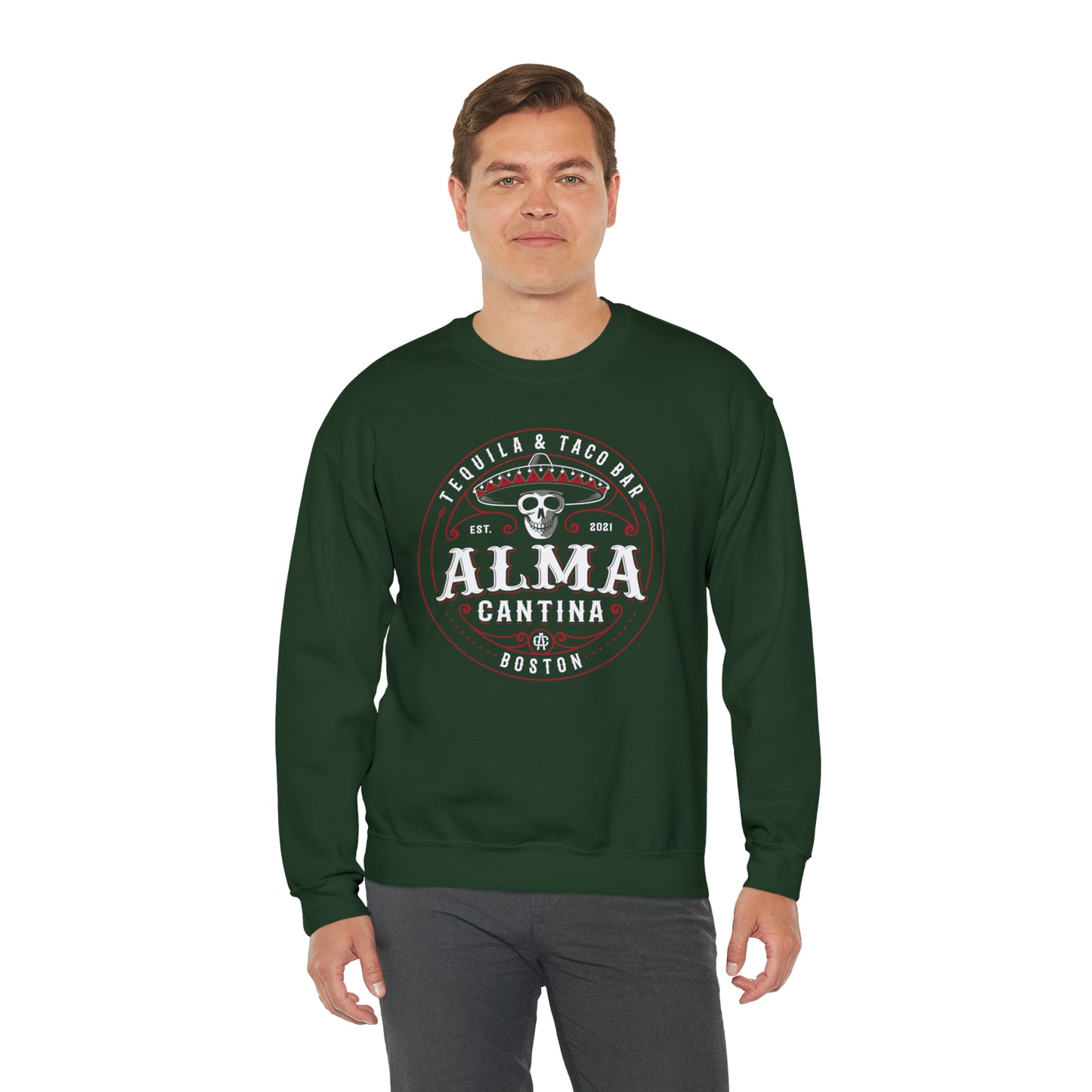Man wearing a dark green crewneck sweatshirt with a white and red Alma Cantina skull and sombrero graphic print.