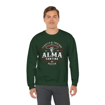 Man wearing a dark green crewneck sweatshirt with a white and red Alma Cantina skull and sombrero graphic print.
