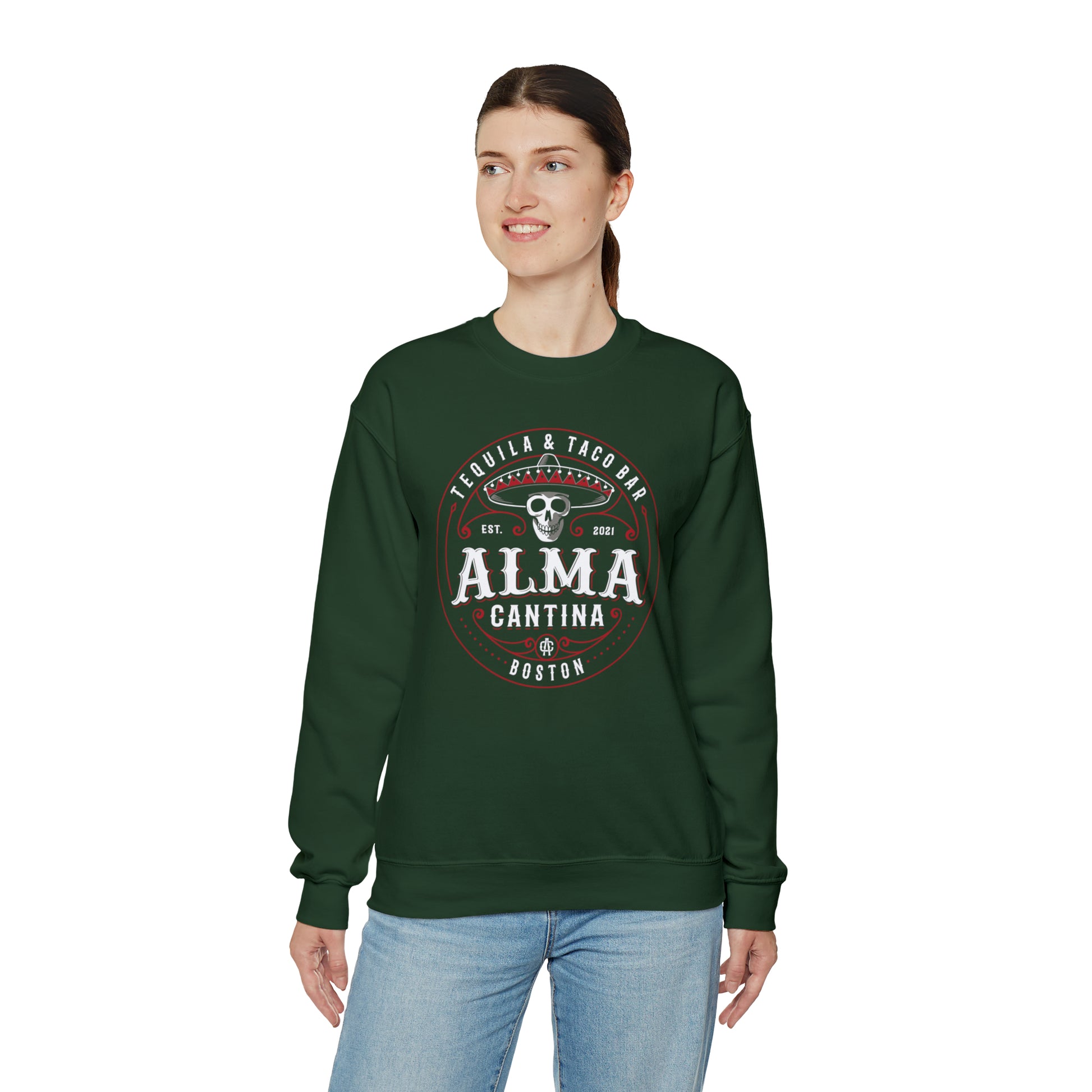 Woman wearing a dark green crewneck sweatshirt with a white and red Alma Cantina skull logo print.