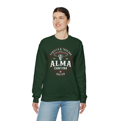 Woman wearing a dark green crewneck sweatshirt with a white and red Alma Cantina skull logo print.