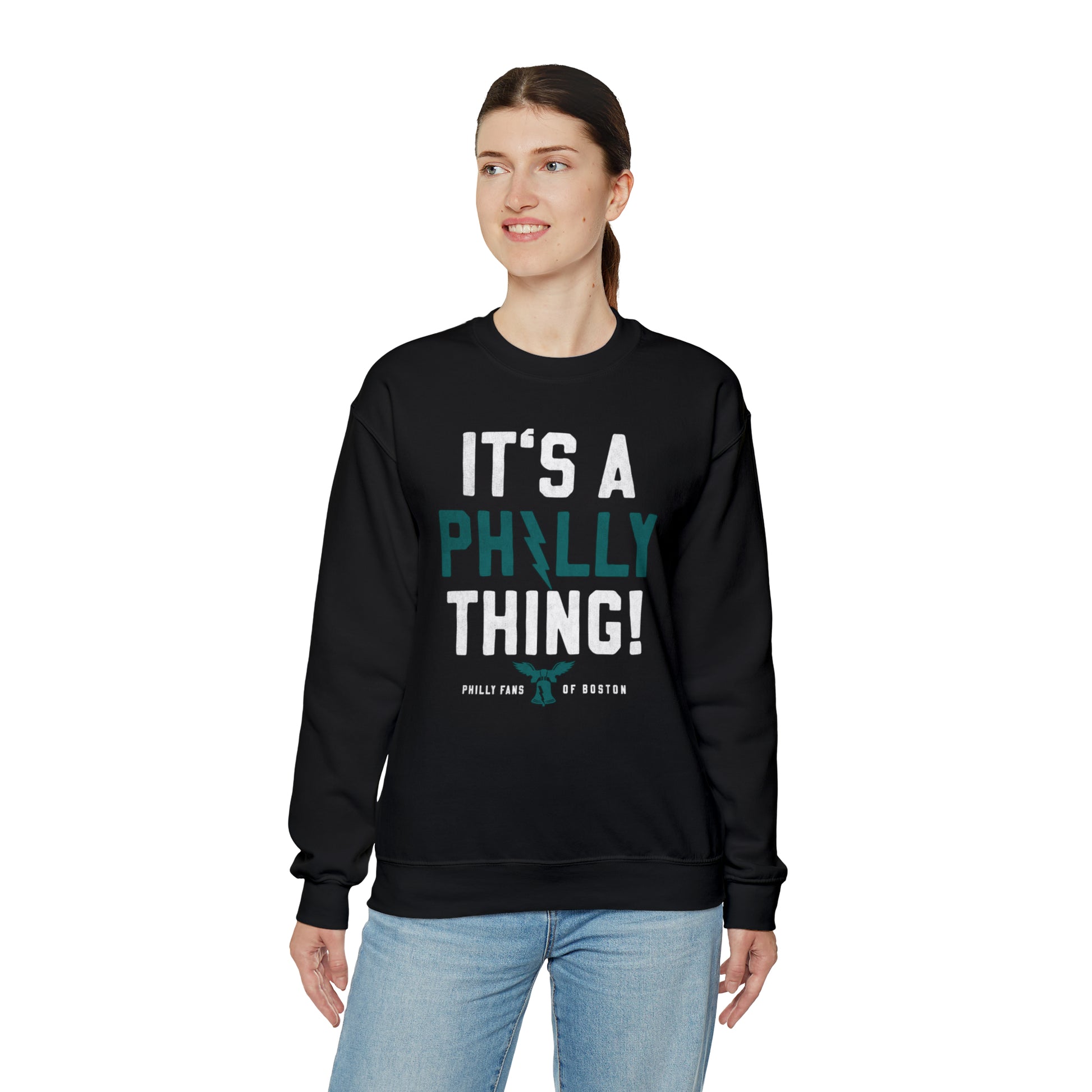Woman wearing a black heavy blend crewneck sweatshirt with It's A Philly Thing graphic print and ribbed collar.