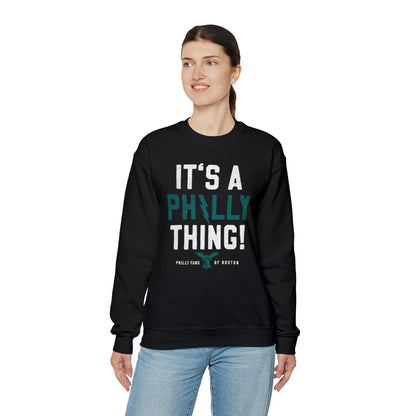 Woman wearing a black heavy blend crewneck sweatshirt with It's A Philly Thing graphic print and ribbed collar.