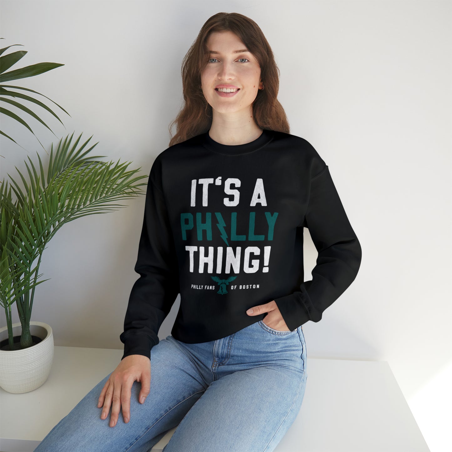 Woman wearing a black crewneck sweatshirt with It's a Philly Thing text, featuring a ribbed collar and loose fit.