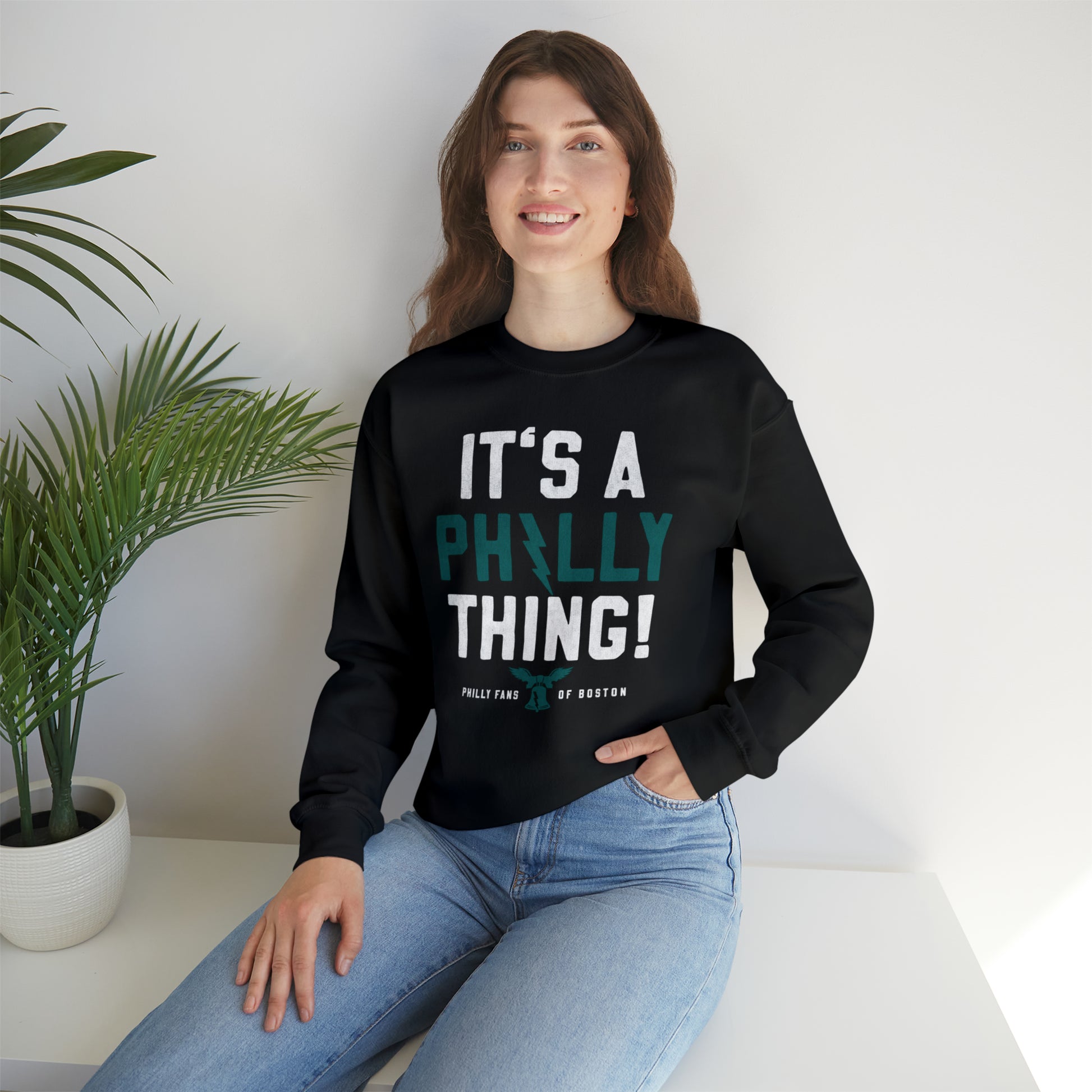 Woman wearing a black crewneck sweatshirt with It's a Philly Thing text, featuring a ribbed collar and loose fit.