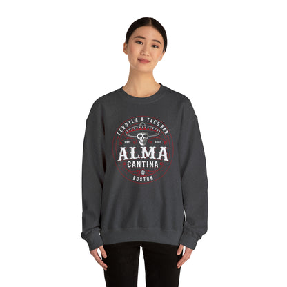 Woman wearing a dark gray heavy blend crewneck sweatshirt with a white and red Alma Cantina skull logo graphic.
