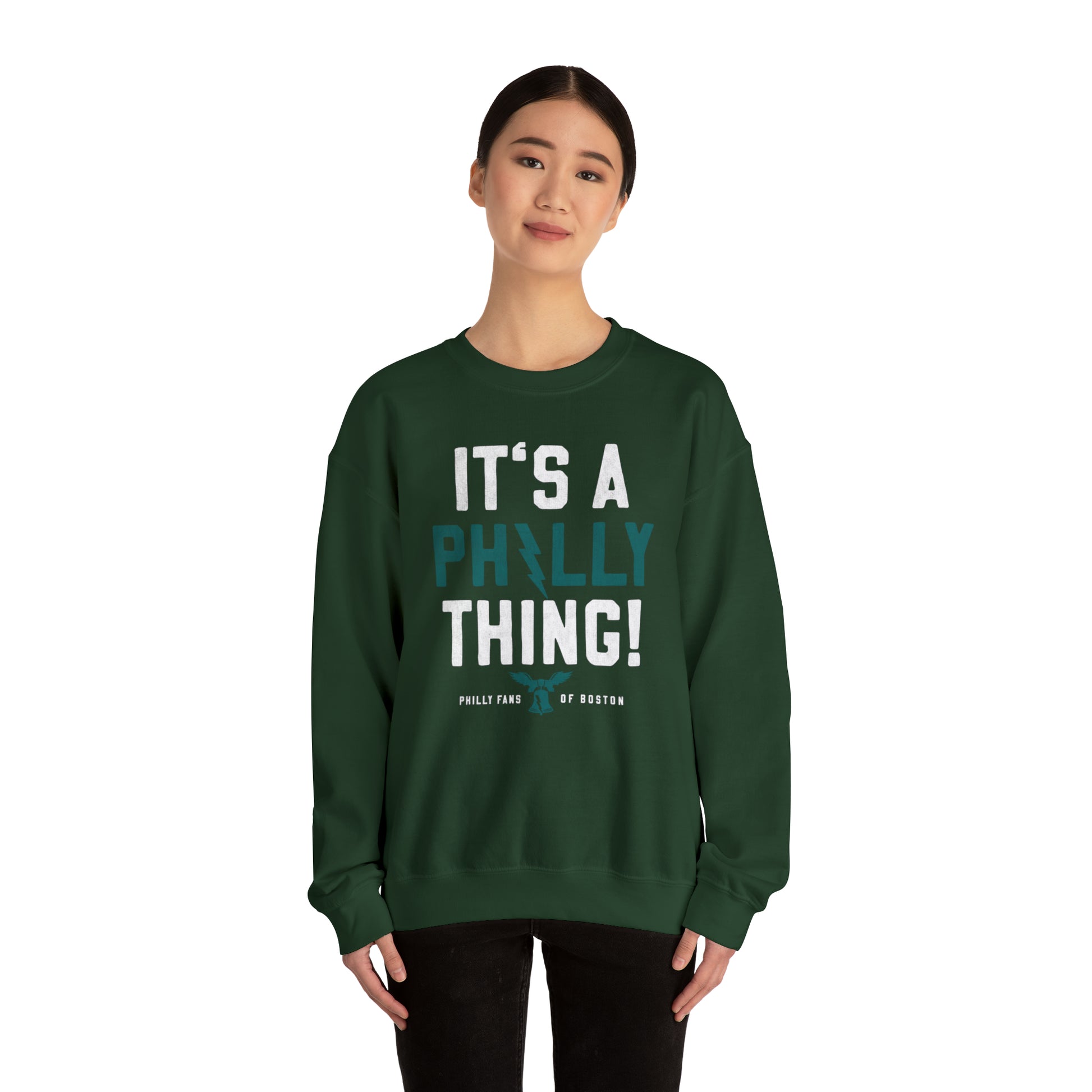 Woman wearing a dark green heavy blend crewneck sweatshirt with white and teal It's a Philly Thing graphic print.