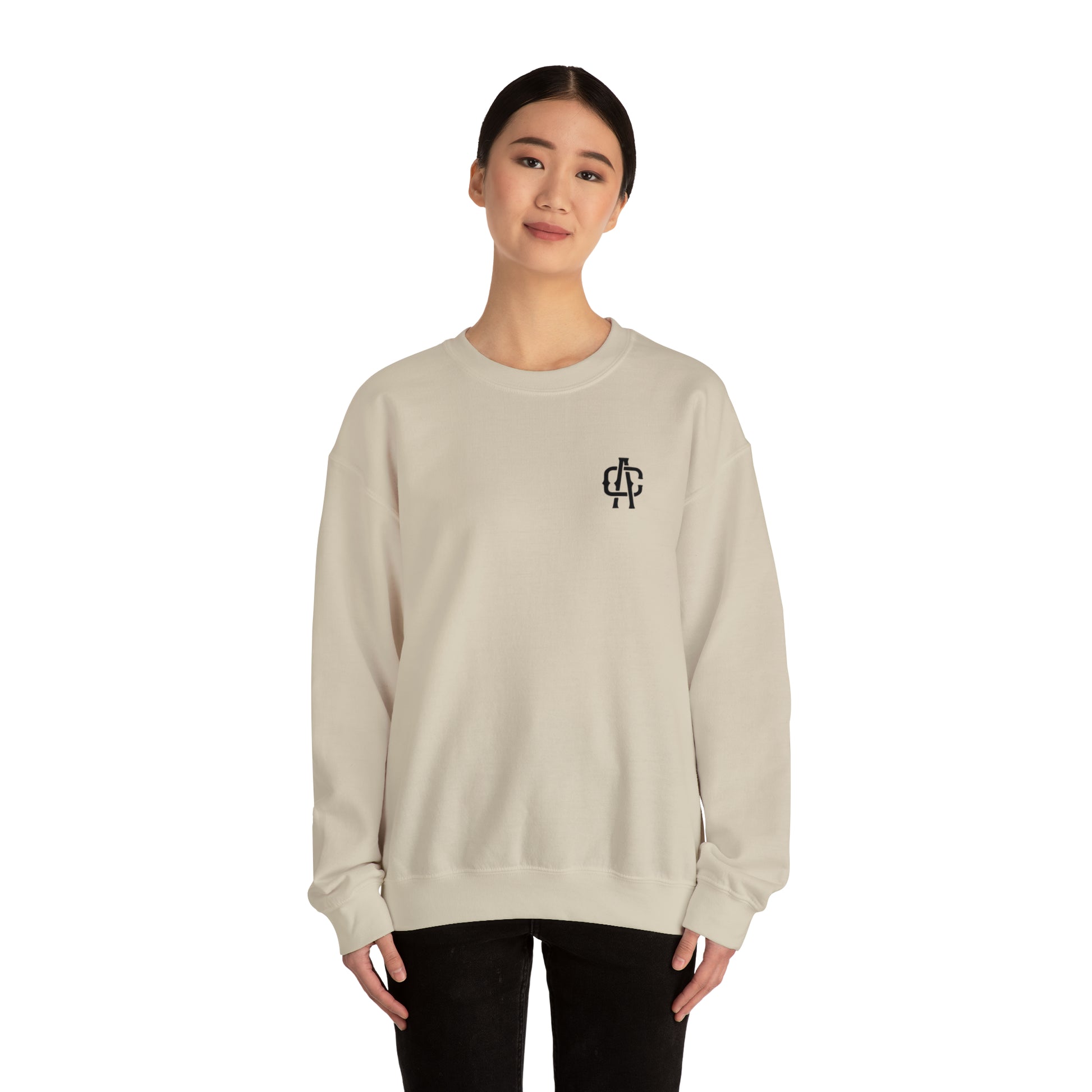 Woman wearing a sand-colored, loose-fit heavy blend crewneck sweatshirt with a small black logo on the chest.