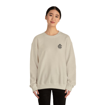 Woman wearing a sand-colored, loose-fit heavy blend crewneck sweatshirt with a small black logo on the chest.