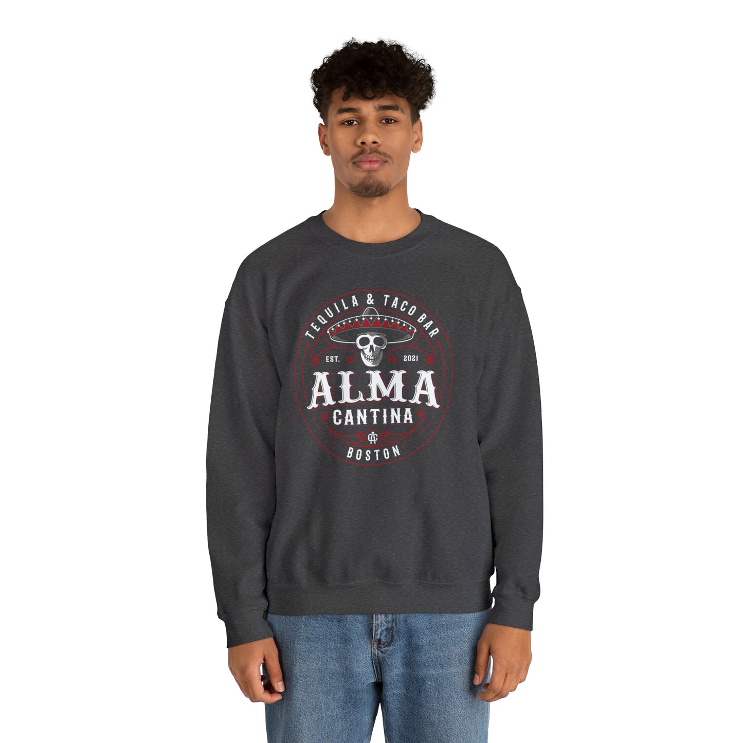 Man wearing a dark gray heavy blend crewneck sweatshirt with a circular Alma Cantina skull and sombrero graphic.