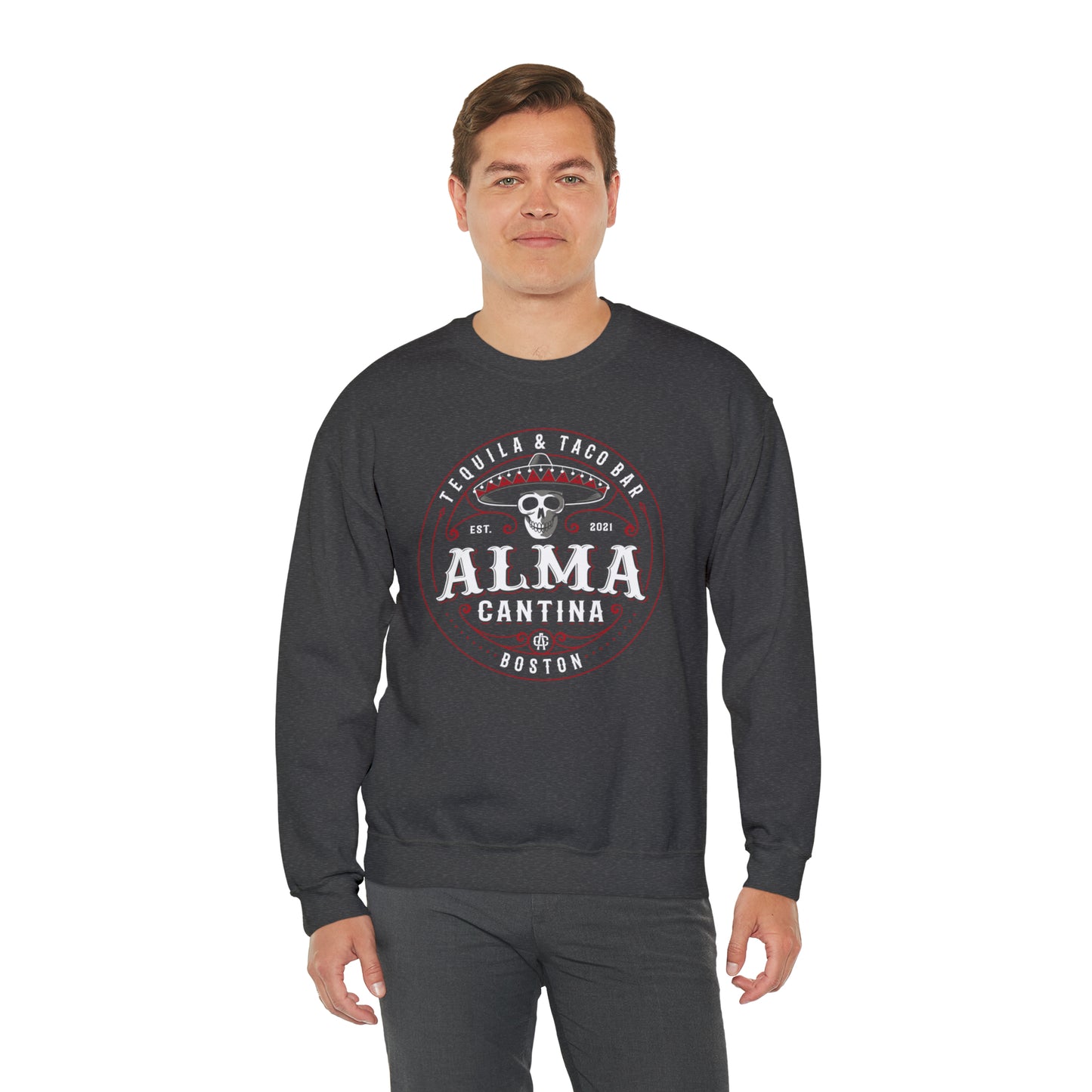 Man wearing a dark gray heavy blend crewneck sweatshirt with a white and red Alma Cantina skull logo graphic.