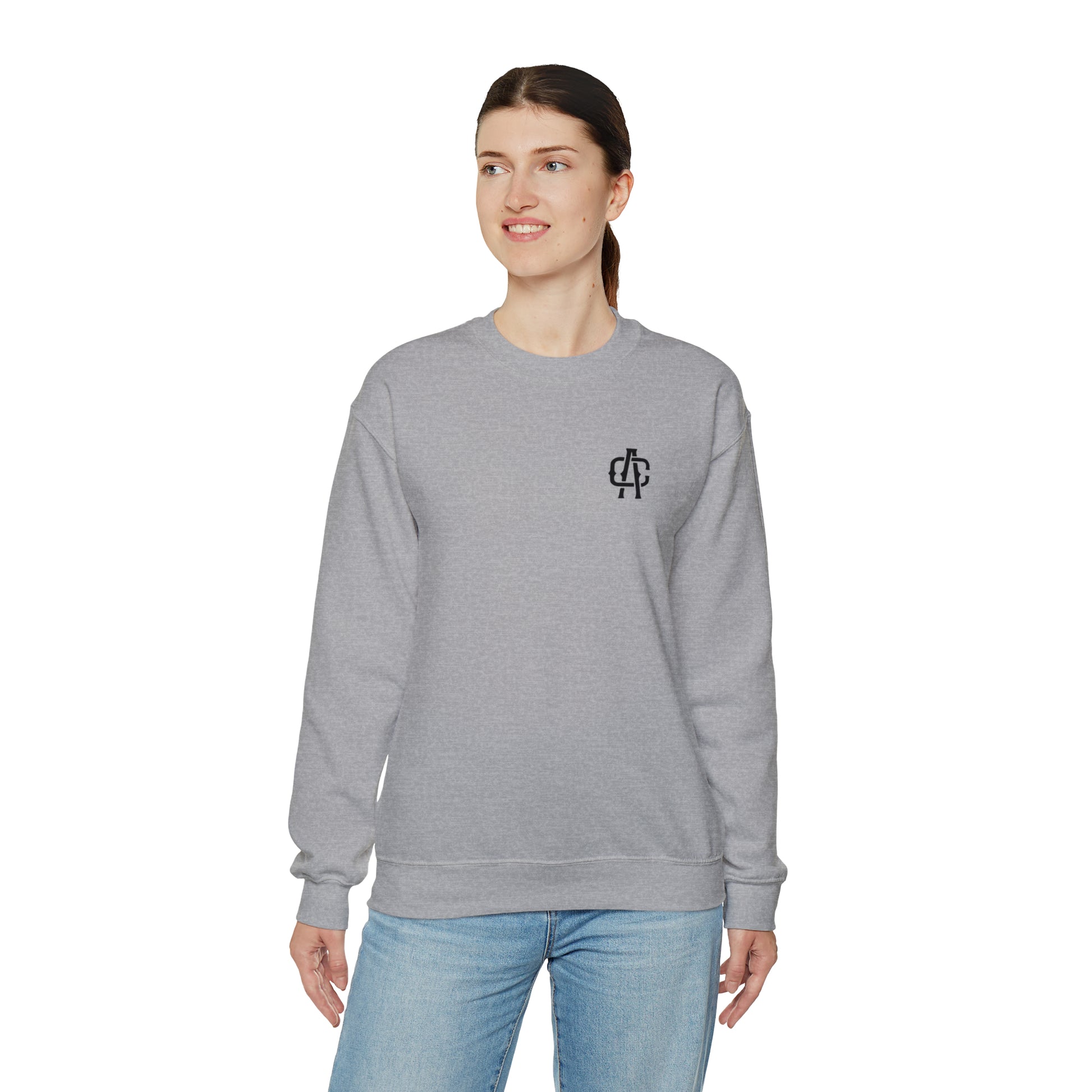 Woman wearing a grey, loose-fit heavy blend crewneck sweatshirt with a ribbed collar and small black chest logo.