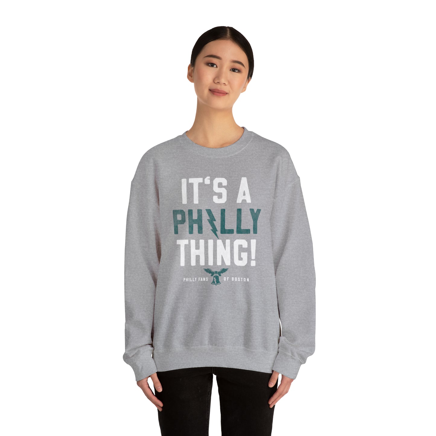 Woman wearing a grey heavy blend crewneck sweatshirt with It's a Philly Thing text and a bell graphic.