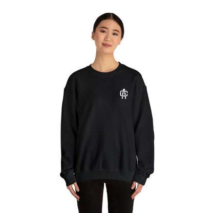 Woman wearing a black heavy blend crewneck sweatshirt with a small white logo on the chest.