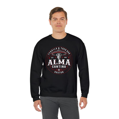 Man wearing a black crewneck sweatshirt with a white and red Alma Cantina skull and sombrero graphic print.