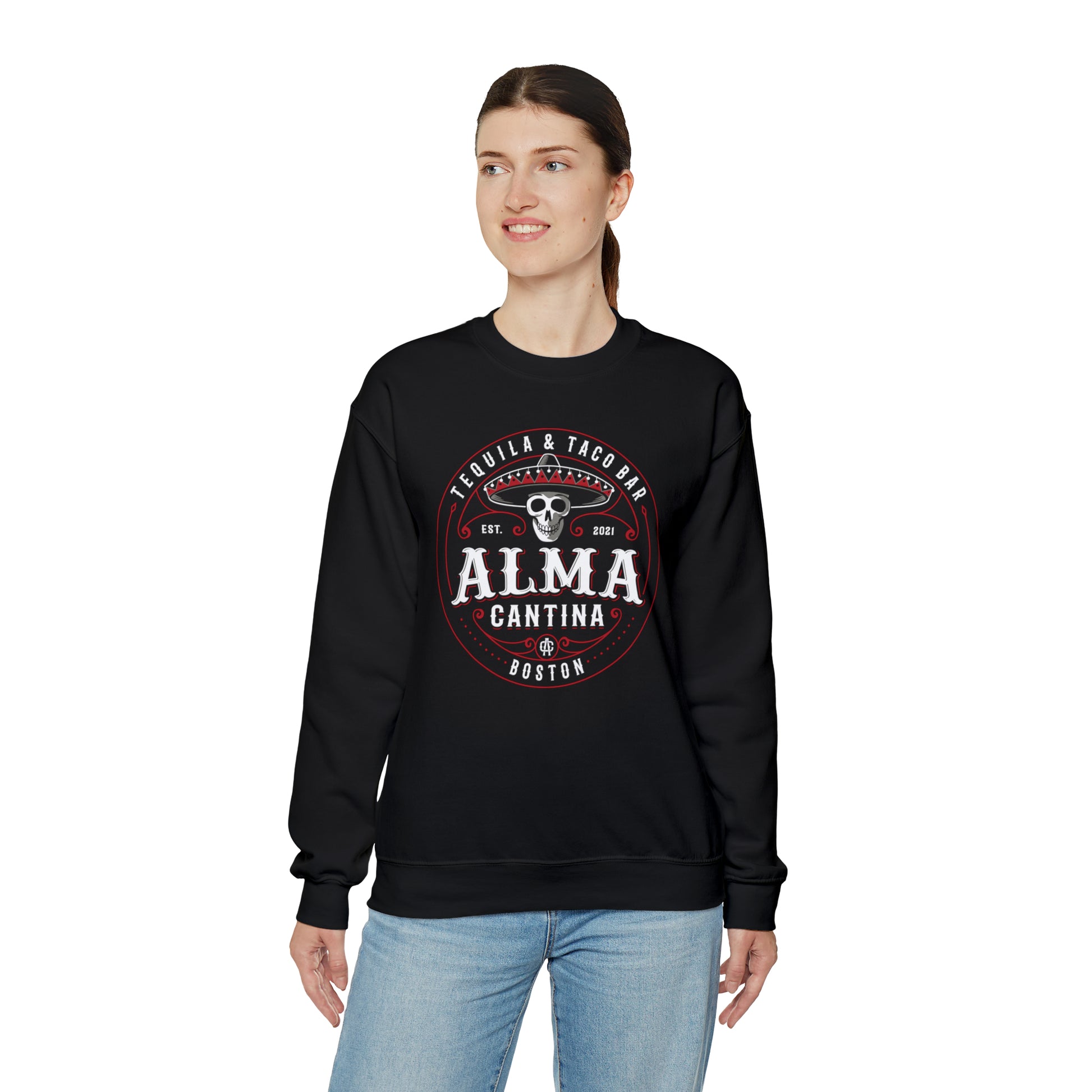 Woman wearing a black heavy blend crewneck sweatshirt featuring a graphic of a skull in a sombrero for Alma Cantina.