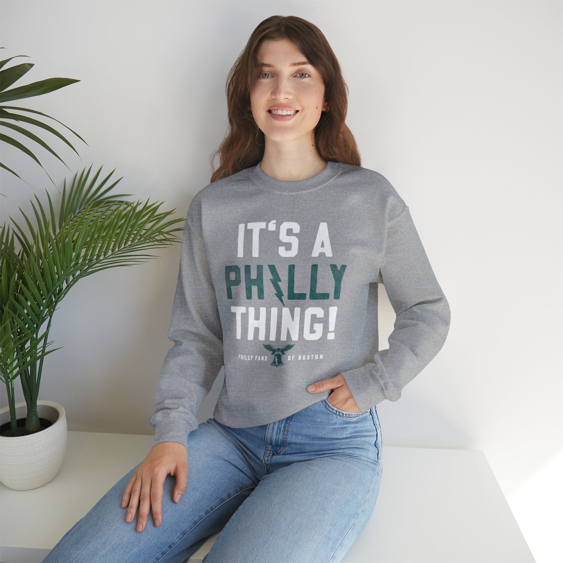 Woman wearing a grey crewneck sweatshirt with It's a Philly Thing text, featuring a ribbed collar and loose fit.