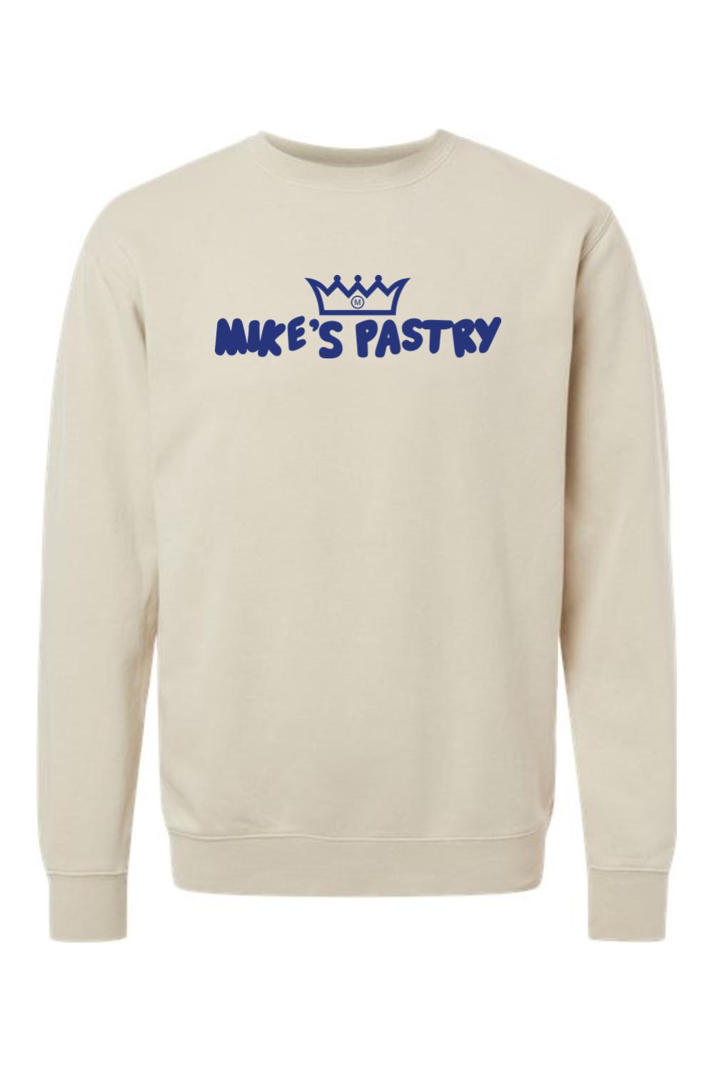 Beige pigment-dyed crewneck sweatshirt featuring a blue Mike's Pastry logo with a crown icon on the chest.