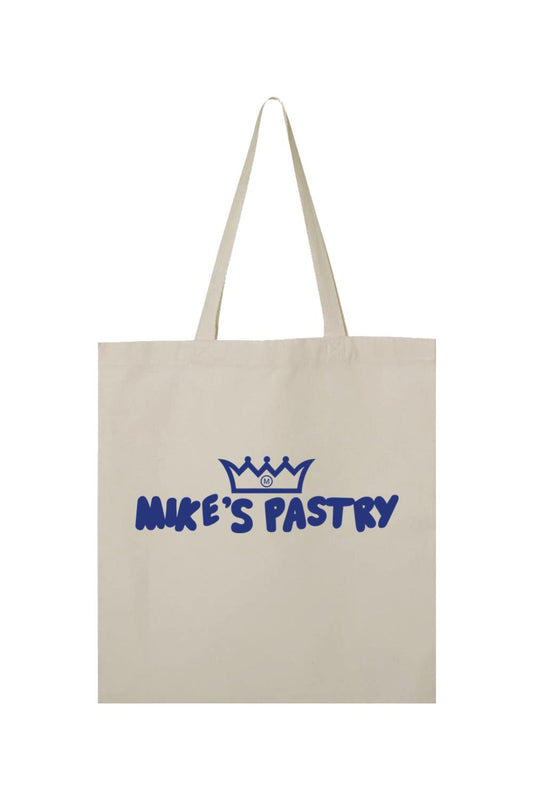 Beige canvas tote bag featuring a blue Mike's Pastry logo with a crown icon and dual shoulder straps.
