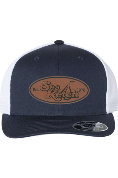 Navy and white trucker cap with a brown oval leather patch featuring the Sea Ketch logo and a Flexfit 110 sticker.