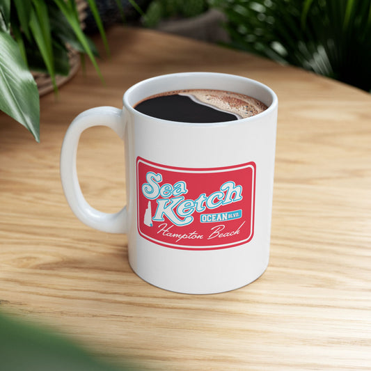 White ceramic mug featuring a red Sea Ketch Hampton Beach logo with a New Hampshire map on a wooden table.