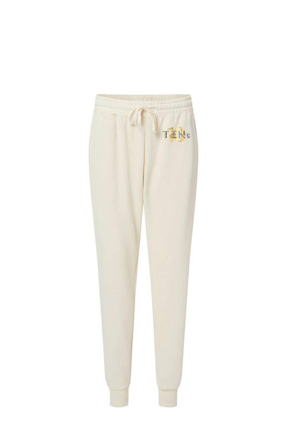 Cream-colored cotton sweatpants with a drawstring waist, ribbed cuffs, and a gold Tens Show Club logo on the hip.