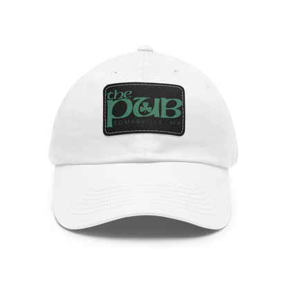 White unstructured dad hat featuring a black faux leather patch with The Pub Somerville green logo.