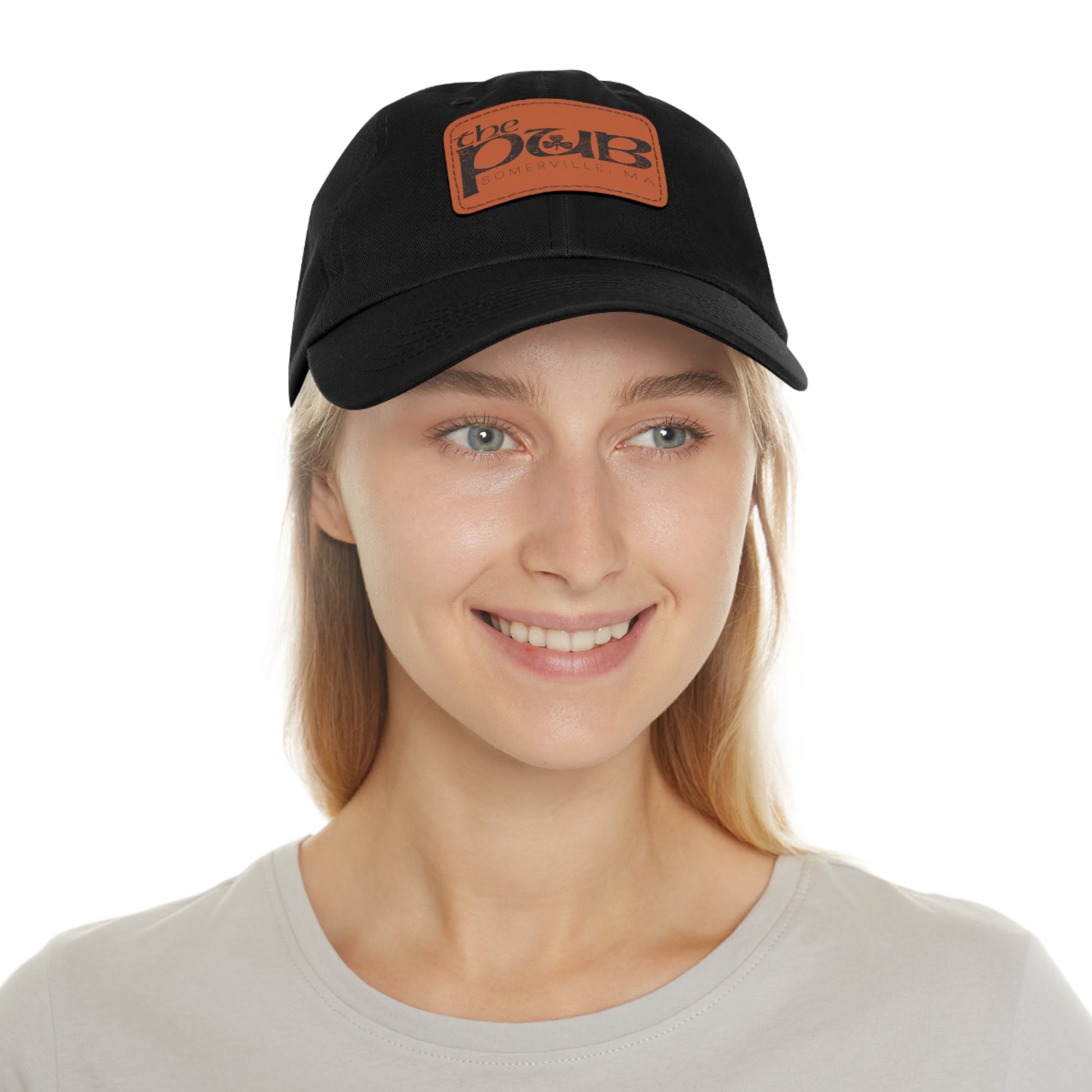 Black unstructured dad hat with a brown faux leather patch featuring The Pub Somerville logo on a woman.